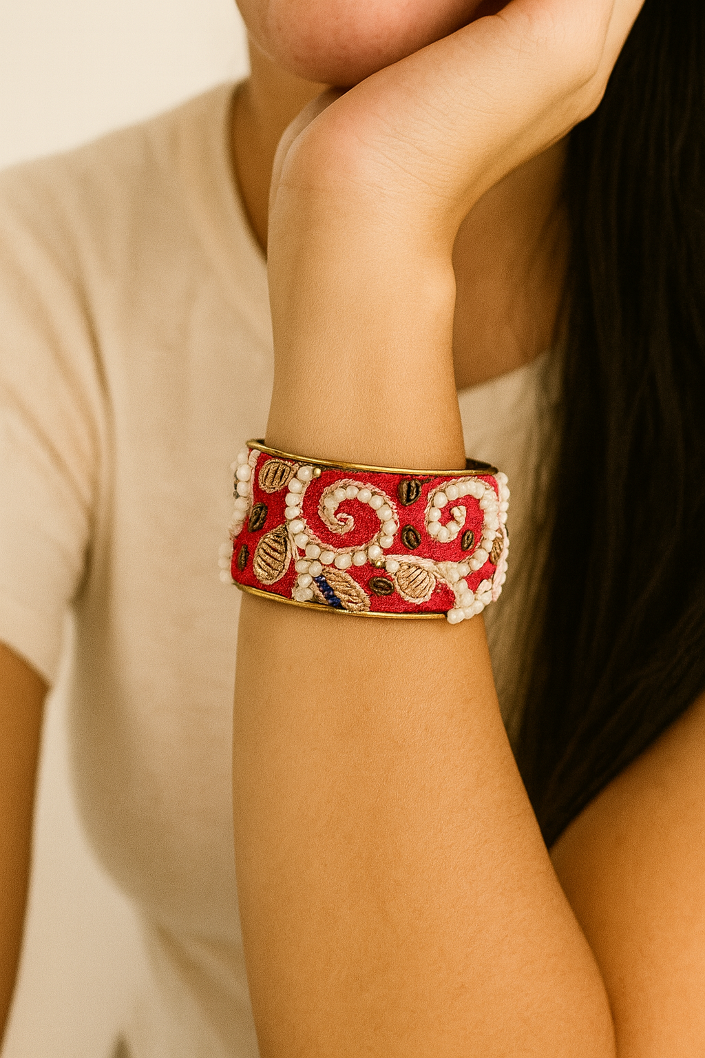 Close-up of a model wearing the Selene 1-Inch brass cuff bracelet by Redd Dott Jewelry, featuring rich red embroidery with ivory beading and gold stitched accents on a slim brass cuff, highlighting the intricate texture and handcrafted bracelet detail, handcrafted in Shreveport, LA by Redd Dott Jewelry.