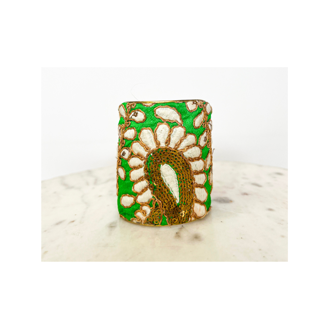 Green Gina cuff bracelet standing upright on marble, showcasing embroidered white petals encircling a gold paisley center, a distinctive handmade bracelet, handcrafted in Shreveport, LA by Redd Dott Jewelry.
