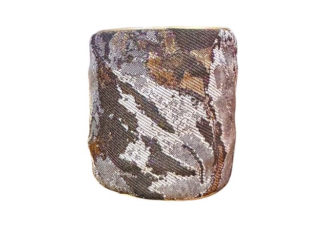 Wide stamped cuff bracelet with an abstract metallic pattern in shimmering bronze, set on a crisp white backdrop. The cuff shows a distinctive textured surface that catches the light.