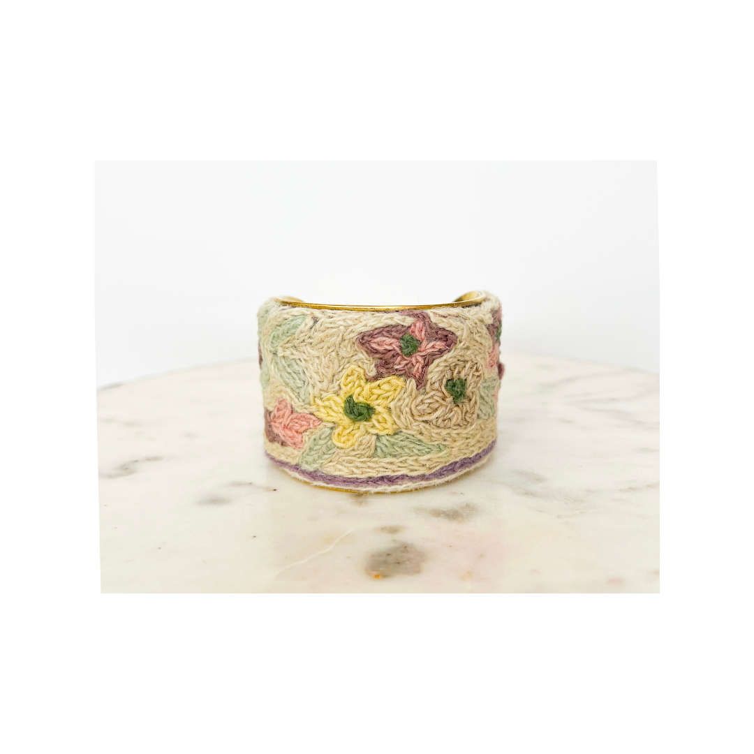 Wide, embroidered floral cuff bracelet with multicolored flowers on a light beige background, displayed on a marble surface.