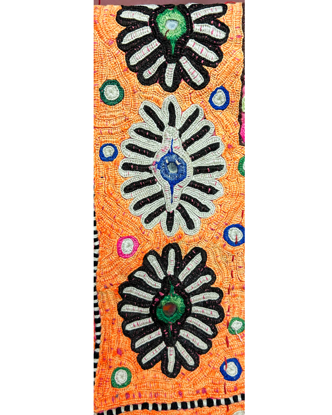 A handcrafted custom stamped cuff bracelet by Redd Dott Jewelry featuring orange vintage kaftan fabric with bold embroidered motifs and mirror accents. A vibrant and textural vintage brass bracelet.