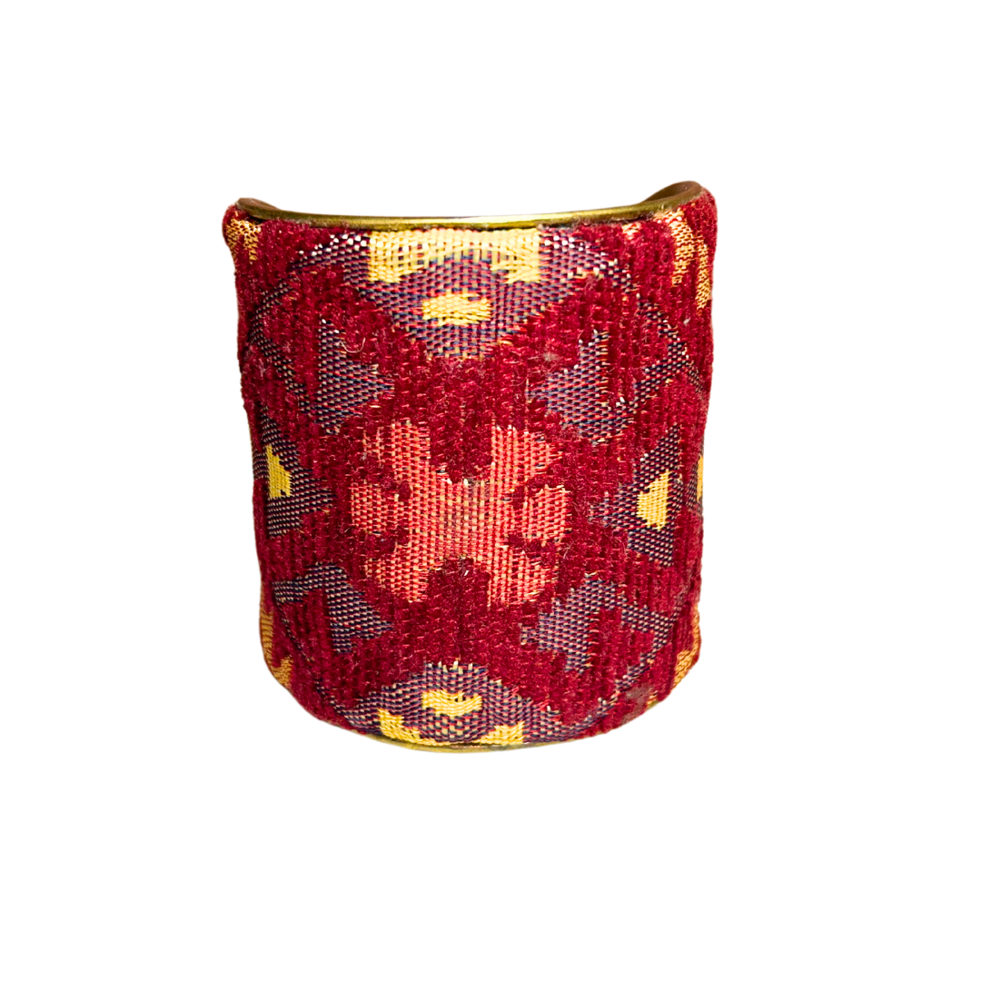 A wide, handmade brass cuff bracelet, crafted and stamped in Shreveport, LA. with a red, gold, and maroon fabric over a vintage brass base.