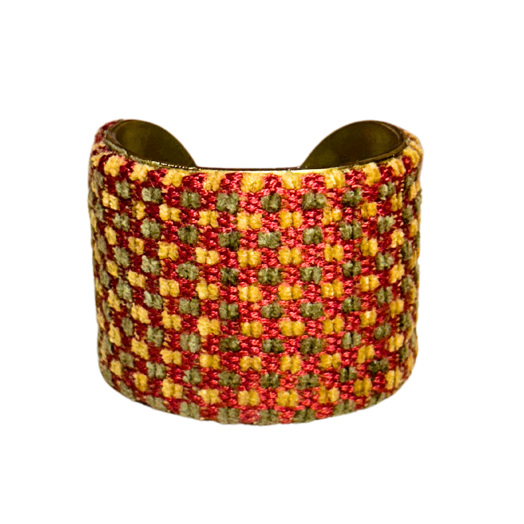 A handmade brass cuff bracelet from Redd Dott Jewelry, crafted and stamped in Shreveport, LA. Features a raised red, gold, and olive green checkered pattern with a rustic cuff bracelet feel over a vintage brass base.