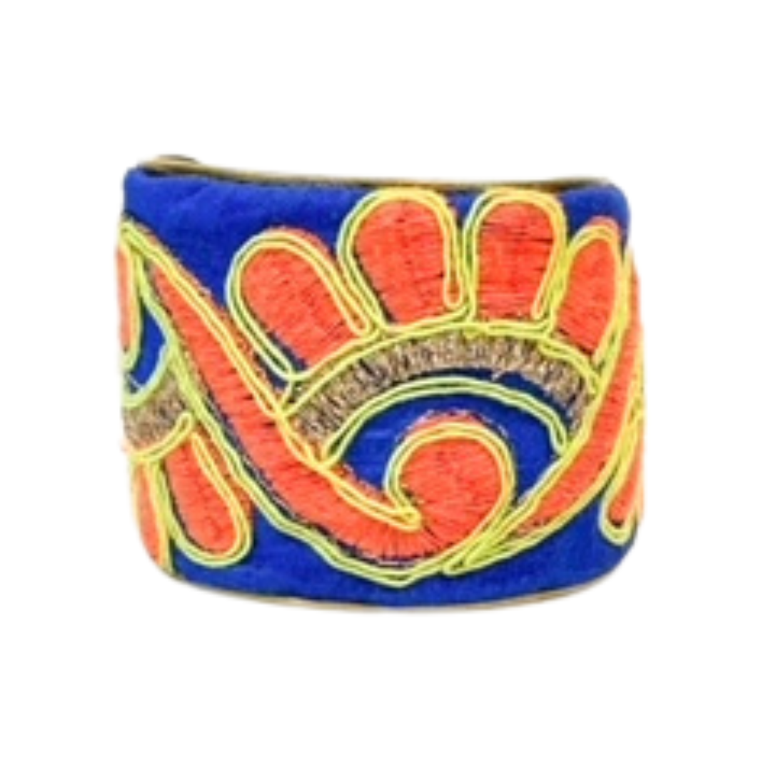 A studio image of a one of a kind jewelry brass cuff bracelet for women in 1-inch and 2-inch widths, wrapped in royal-blue fabric embroidered with coral-pink petals and yellow accents, shown against a white background.