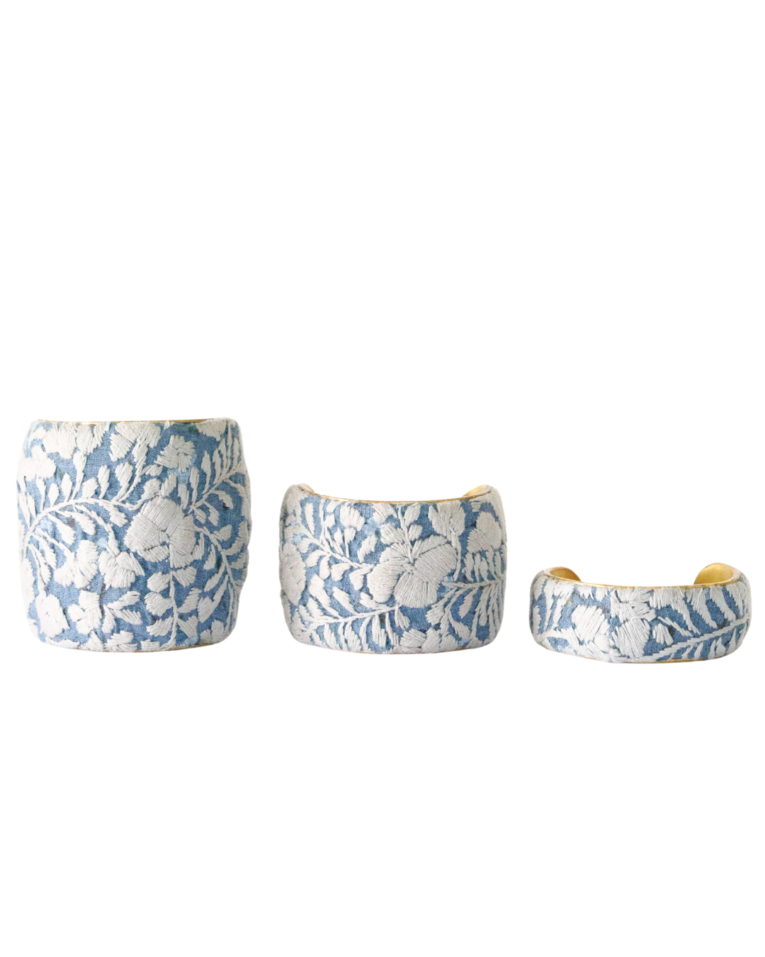 Three Cielo Gris brass cuff bracelets in 1-, 2-, and 3-inch widths with pale blue and ivory embroidery on open-back brass bases.
