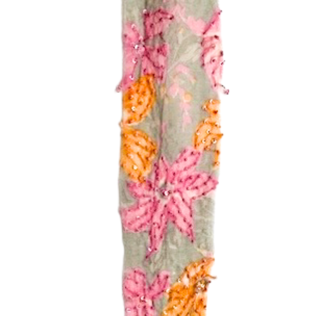 A handcrafted rustic cuff bracelet by Redd Dott Jewelry, featuring an embroidered floral pattern in soft pink and warm orange on a light grey background. Delicate beading and shimmering sequins enhance the intricate textile details,