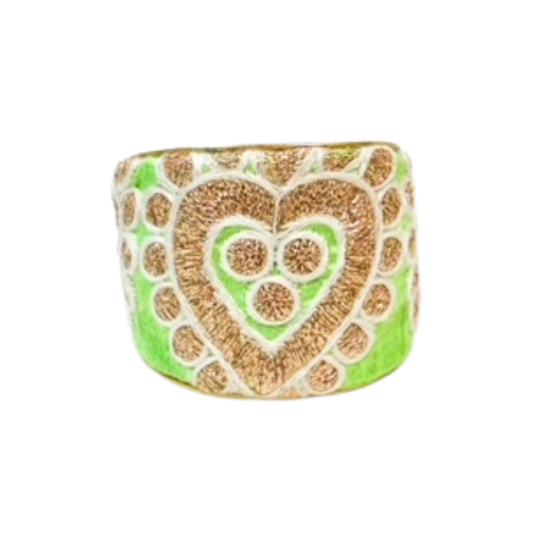 A green and gold embroidered brass cuff bracelet featuring a double-heart motif on a vintage textile background