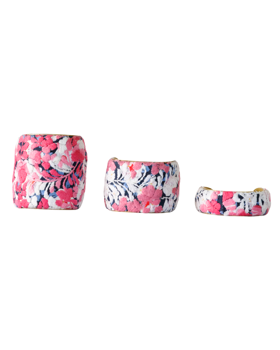Three Flor De Alma brass cuff bracelets in 1-, 2-, and 3-inch widths, showcasing vivid pink and ivory floral embroidery on navy blue fabric.