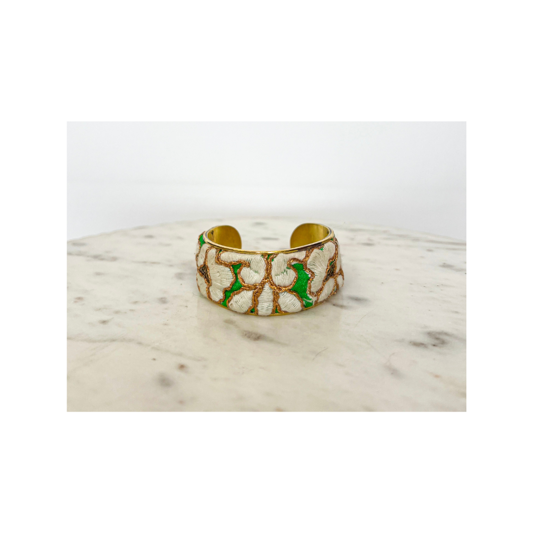 Gina floral cuff bracelet displayed on marble, featuring white petals, gold thread, and green accents on brass, a delicate piece of handcrafted jewelry, handcrafted in Shreveport, LA by Redd Dott Jewelry.