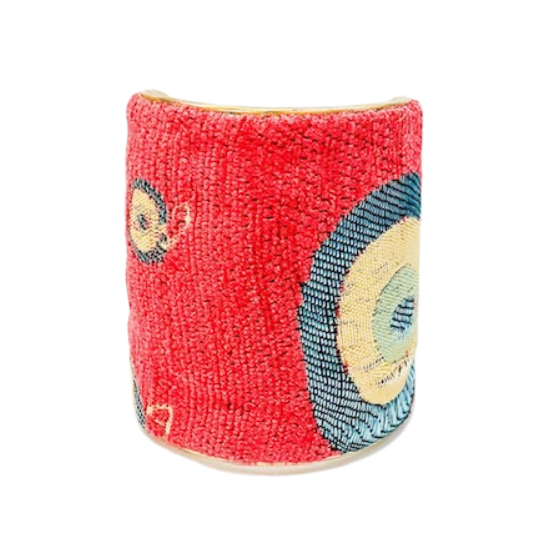 A studio image of a 3-inch brass cuff bracelet for women wrapped in red tapestry fabric featuring concentric circle motifs in teal, mustard, and navy; one of a kind jewelry with a smooth open-back fit.
