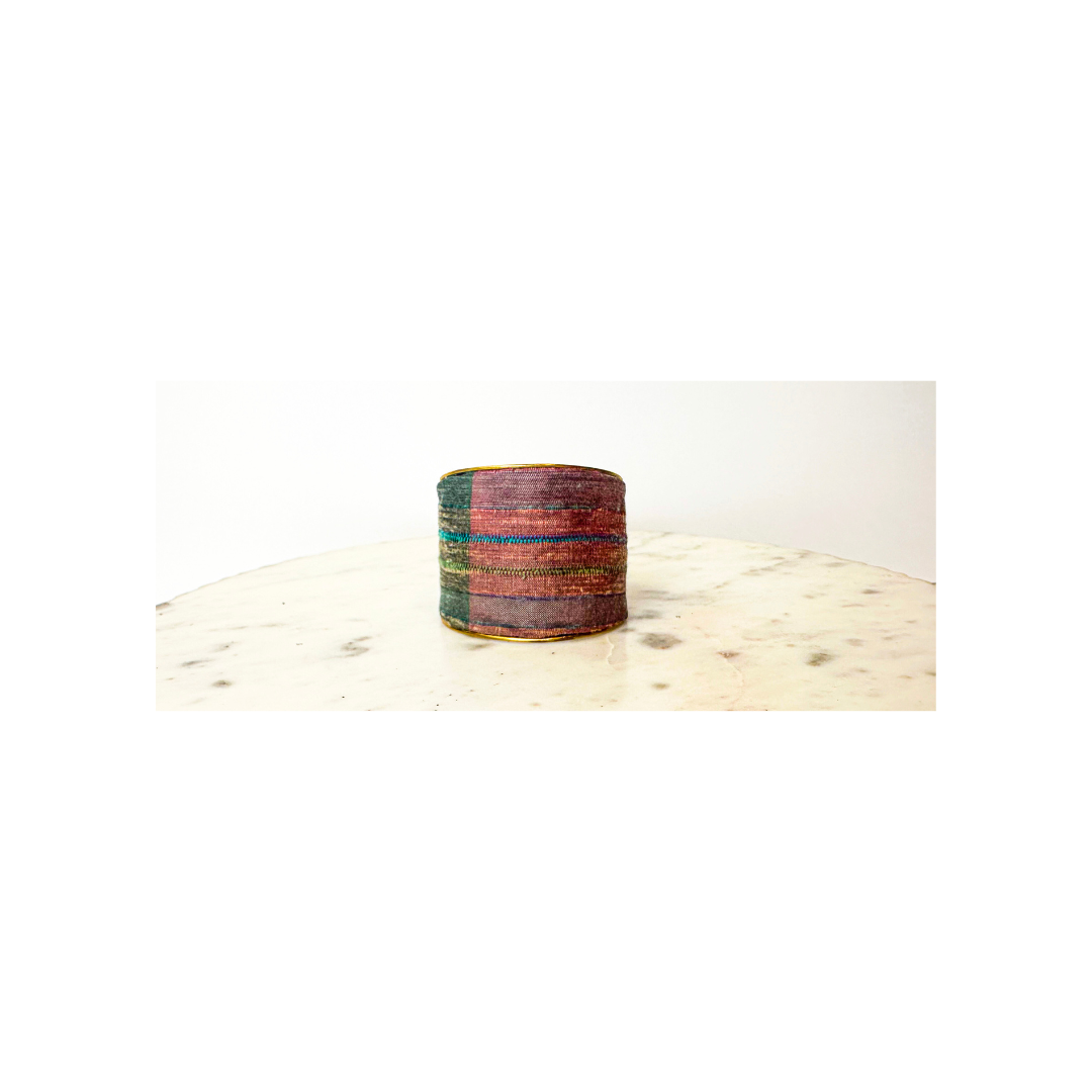 Discover the Judeth Earthly Tapestry cuff: a 2-inch brass cuff bracelet wrapped in dual-tone woven fabric of forest green and magenta with teal and russet accents. This one of a kind jewelry piece for women features an adjustable open-back design. Handmade by Redd Dott Jewelry.