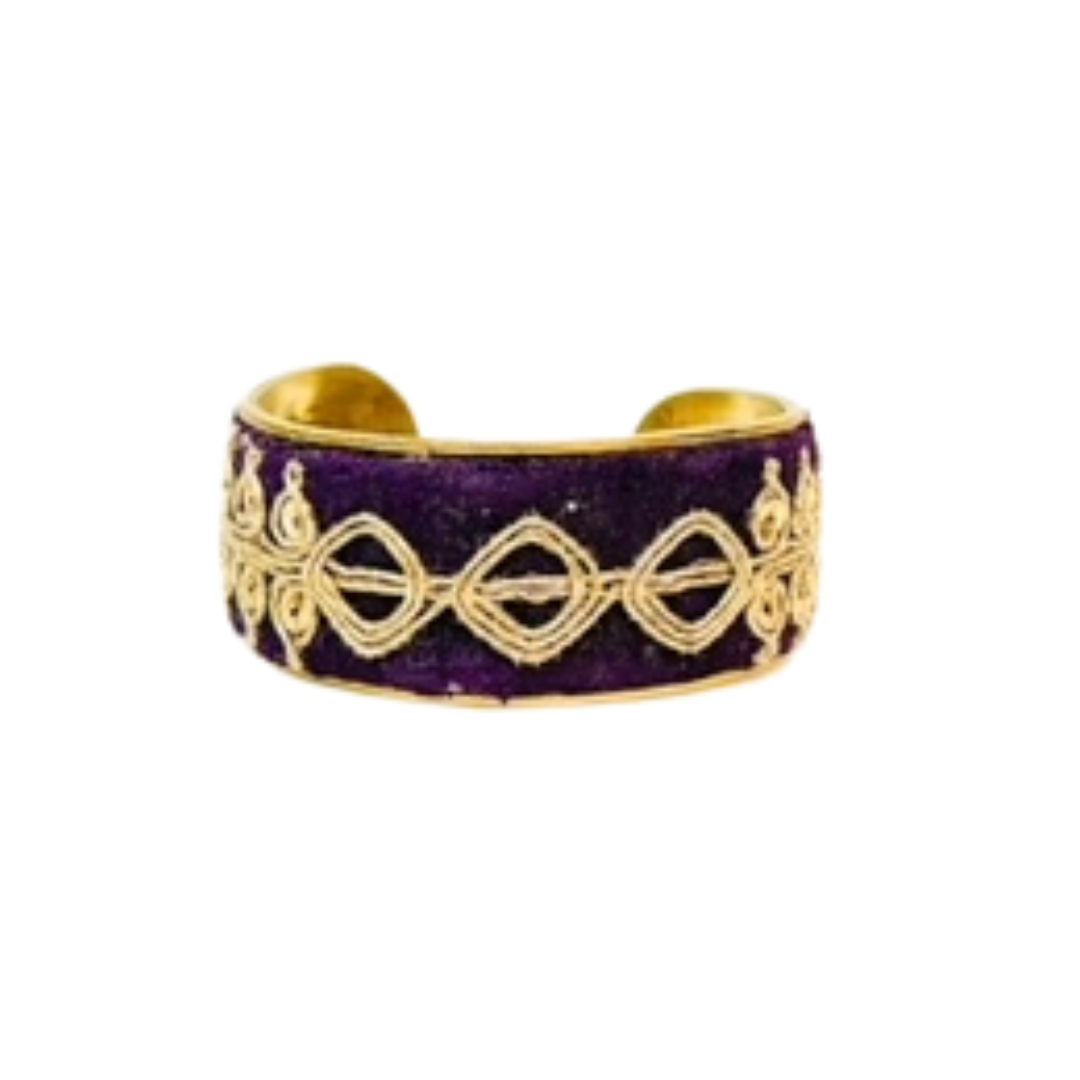 A 1-inch wide brass cuff bracelet wrapped in deep purple velvet and embellished with looping gold filigree embroidery; features an open-back adjustable design and hides a surprise inspirational quote inside.