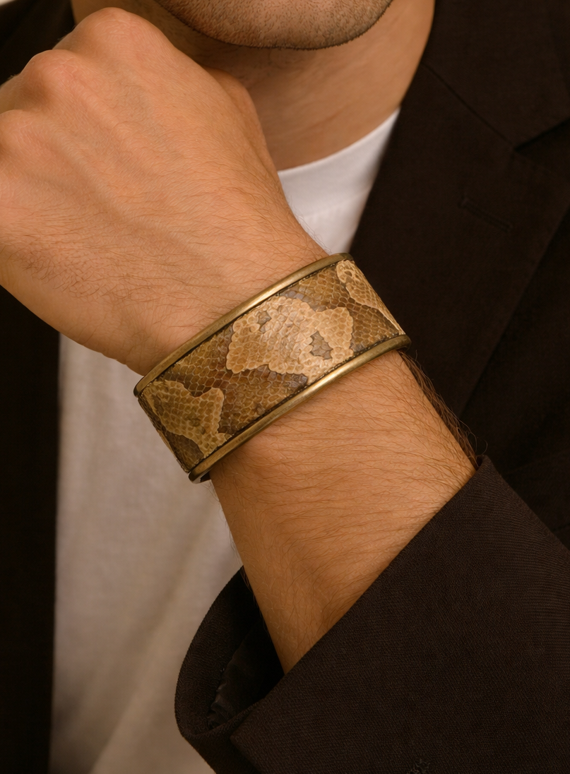 Close-up of a model wearing the men’s 1-Inch copperhead snake skin cuff bracelet by Redd Dott Jewelry, featuring warm tan and brown scale pattern framed in a slim brass cuff, highlighting the natural texture and handcrafted cuff bracelet detail, handcrafted in Shreveport, LA by Redd Dott Jewelry.
