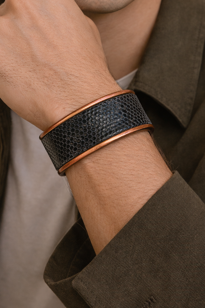 Close-up of a model wearing the men’s 1-inch lizard skin cuff bracelet by Redd Dott Jewelry, showcasing deep black lizard leather with fine rounded scale texture, framed by warm copper-toned brass edges for a bold yet refined cuff bracelet look, handcrafted in Shreveport, LA by Redd Dott Jewelry.