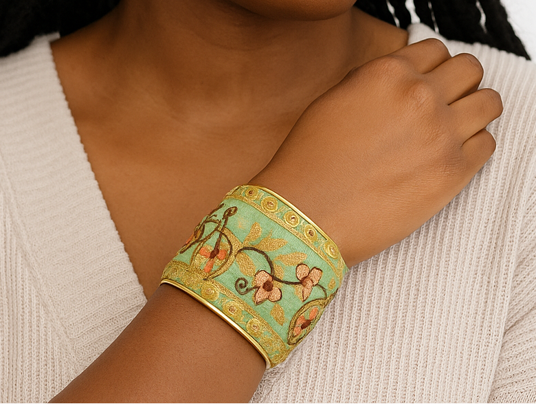 Close-up of a woman wearing the Ambrose Embroidered Bracelet, a green and gold floral statement cuff with intricate threadwork and brass trim, handcrafted in Shreveport, LA by Redd Dott Jewelry.
