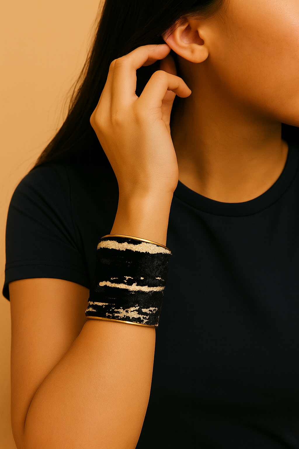 Female model in a black top wearing a 3-inch wide brass cuff bracelet wrapped in black velvet with cream stripe accents on her left wrist. A bold, one of a kind jewelry statement among cuff bracelets for women.