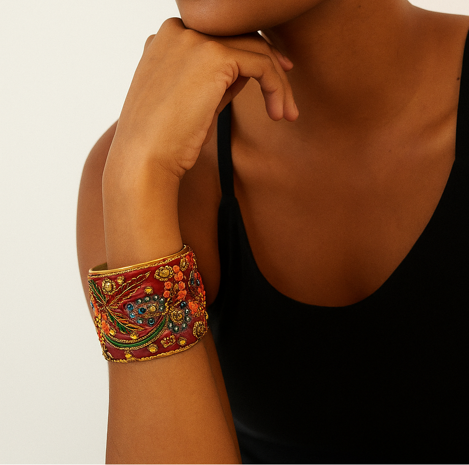 Female model with braided hair wearing a black tank top, showing a 2-inch wide brass cuff bracelet wrapped in red silk sari fabric with gold embroidery and multicolored beadwork on her left wrist. A bold example of one of a kind jewelry and standout cuff bracelets for women.