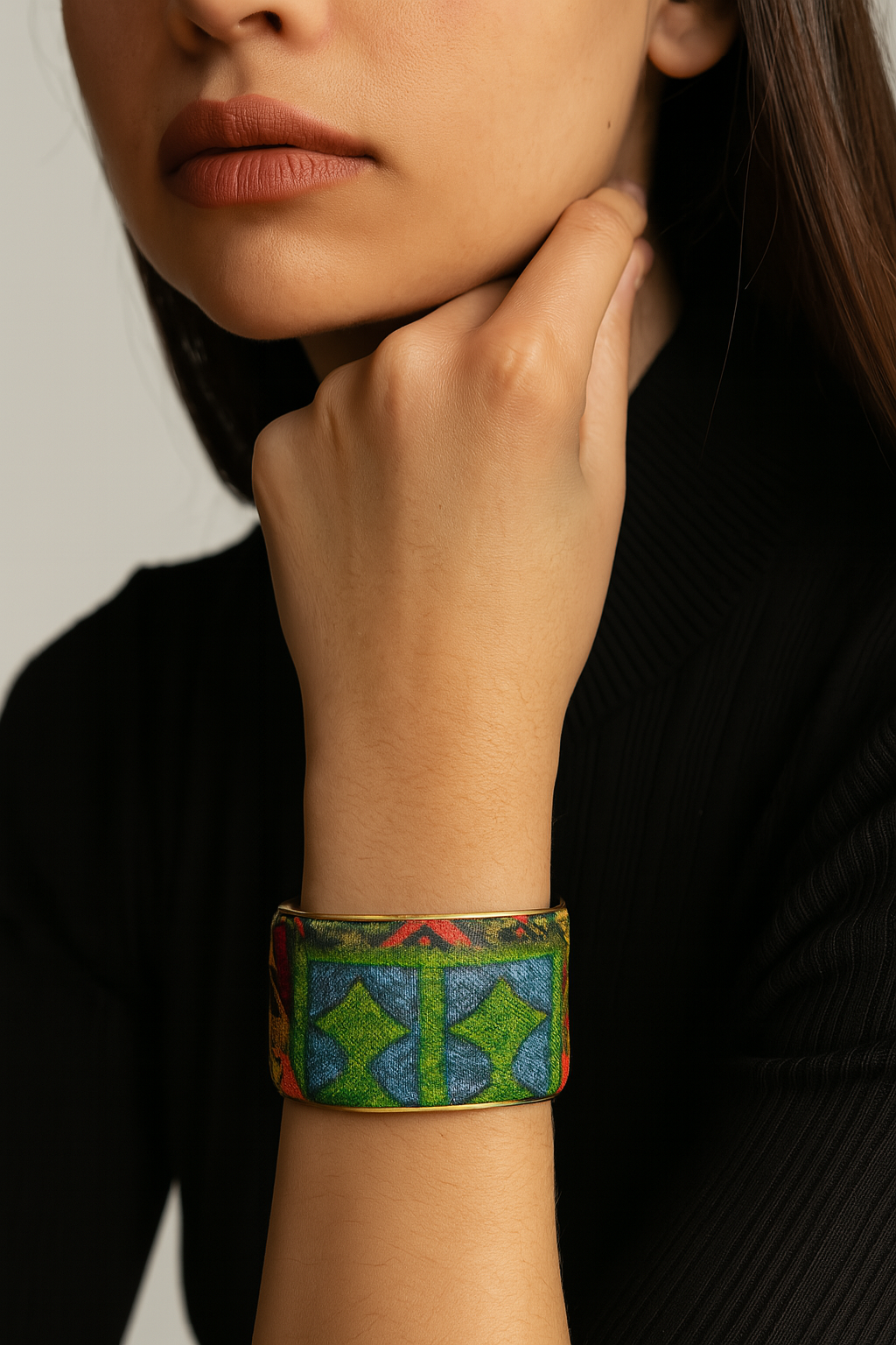 A female model’s wrist adorned with a 2-inch raw brass cuff bracelet featuring vibrant orange mosaic-print fabric with green and blue highlights, a one of a kind jewelry statement for cuff bracelets for women.