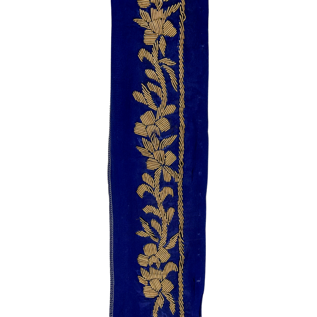 A gold statement bracelet by Redd Dott Jewelry, featuring intricate gold floral embroidery on a deep blue velvet background.
