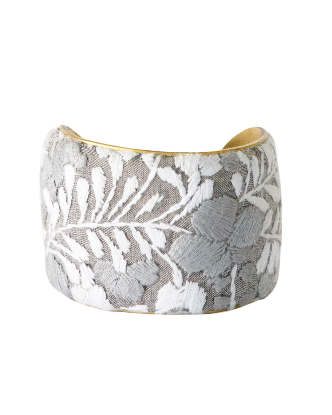 Niebla 2-inch embroidered brass cuff bracelet showing detailed gray and ivory leaf stitching on soft woven fabric with polished brass edges.