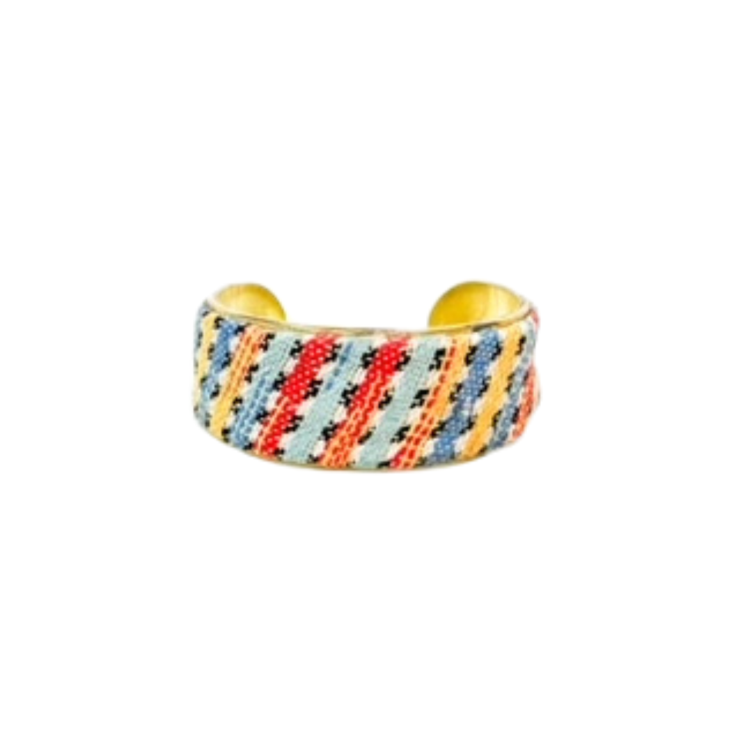 A 1-inch brass cuff bracelet for women wrapped in sunrise-striped woven fabric of red, blue, yellow, and mint with black cross-stitch details, presented on a white background as one of a kind jewelry.