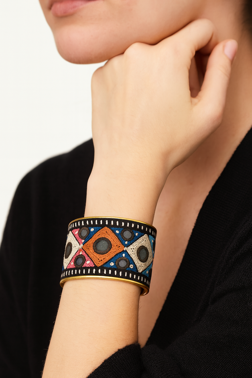 Model wearing the Redd Dott Meghan 2-inch cuff bracelet, designed with bold geometric embroidery in orange, blue, cream, and pink diamond patterns accented with circular black details, all framed in a sleek gold cuff with black trim.