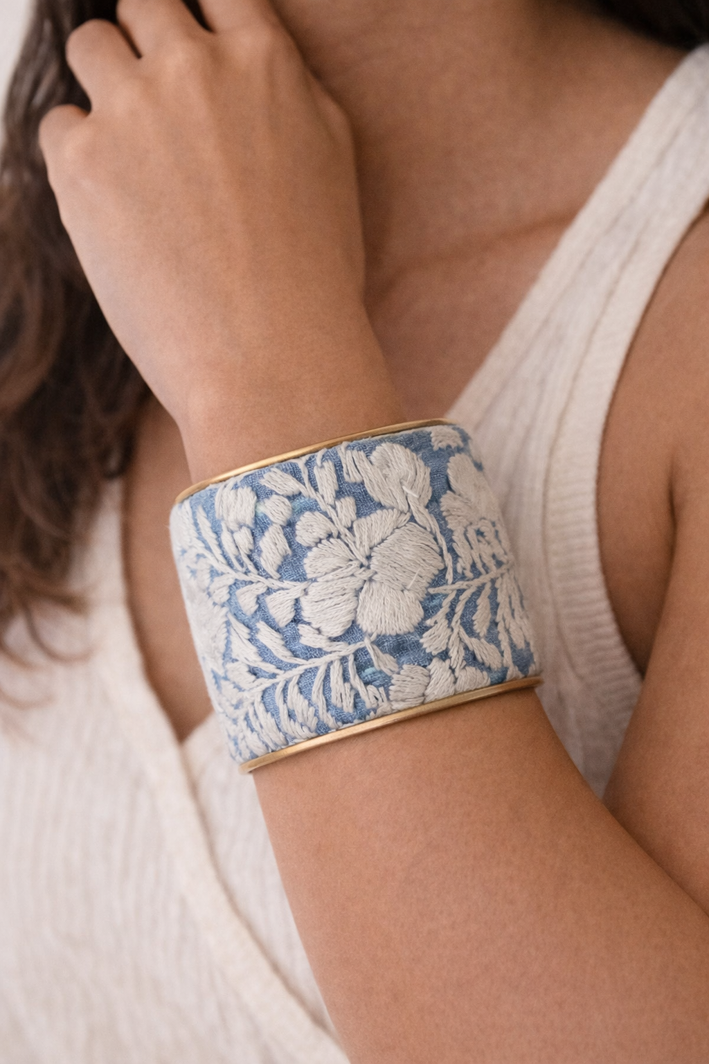 Model Wearing Two-inch Cielo Gris cuff bracelet featuring delicate ivory embroidery on light blue fabric over hand-shaped brass.
