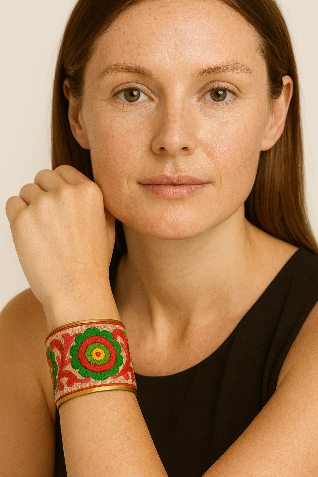 Close-up of a woman wearing the Redd Dott Primrose 2-inch gold cuff bracelet, featuring bold circular floral embroidery in red, green, and yellow with decorative red scroll accents on a neutral base.