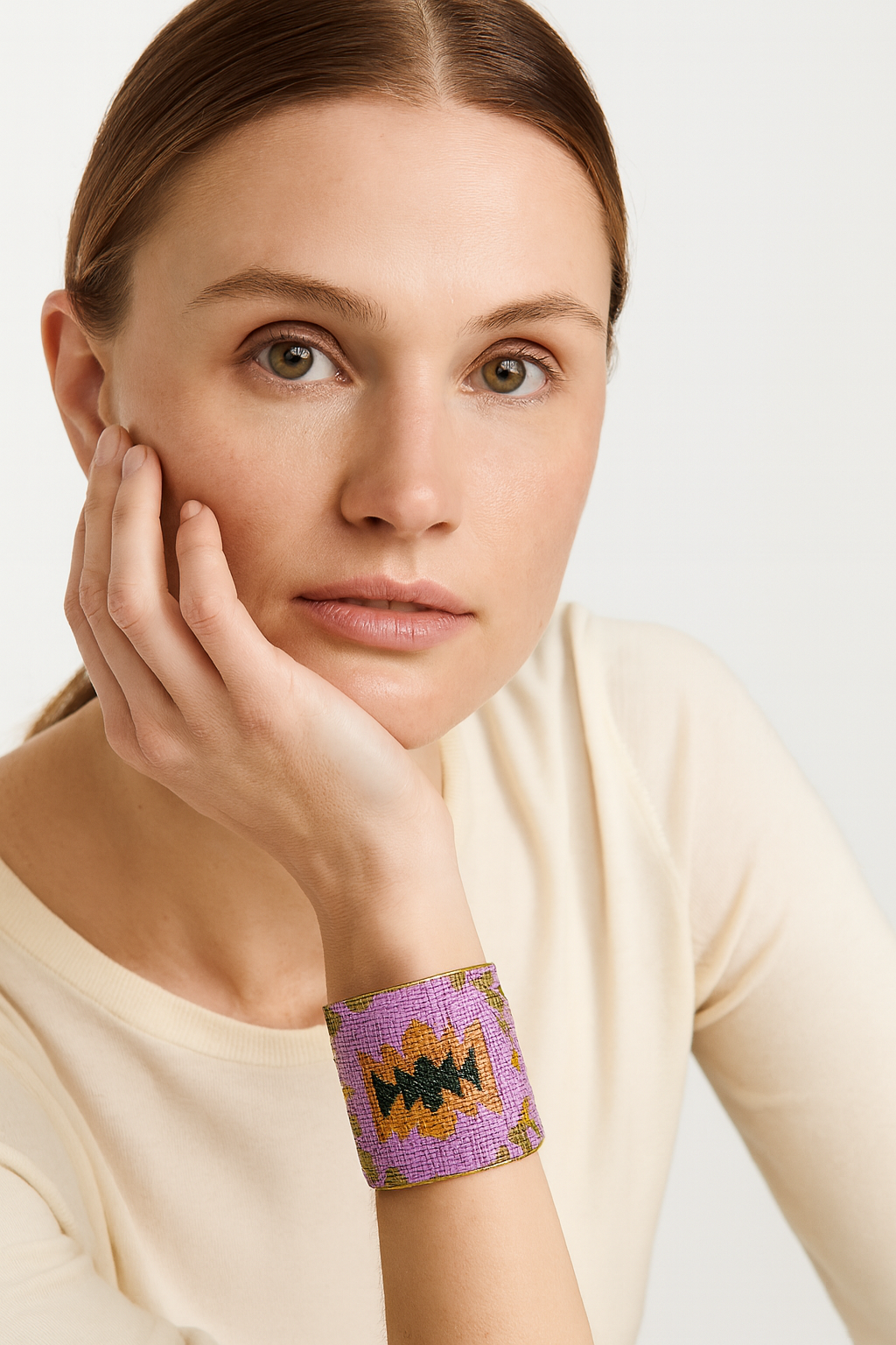 Close-up of a woman wearing the Redd Dott Reina 3-inch gold cuff bracelet, featuring lavender fabric with bold geometric embroidery in mustard yellow, black, and green accents.