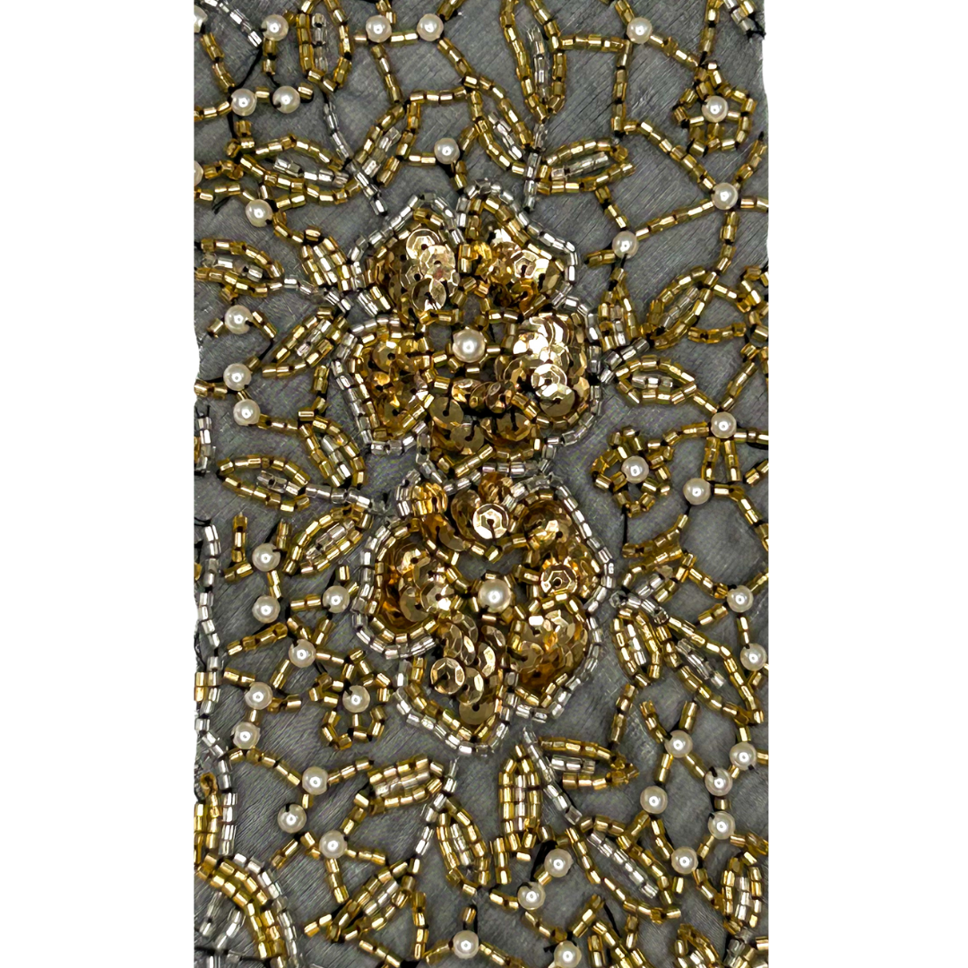 A gold cuff bracelet by Redd Dott Jewelry, featuring intricate floral and lattice beadwork with shimmering gold sequins and pearl accents on a soft gray base.