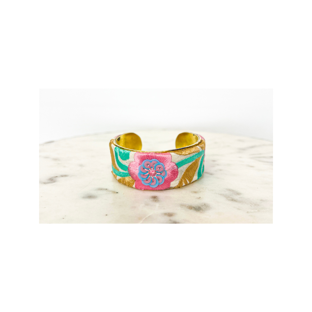 A vibrant turquoise cuff bracelet with a yellow interior and a floral design featuring pink, green, and blue patterns on a light surface.