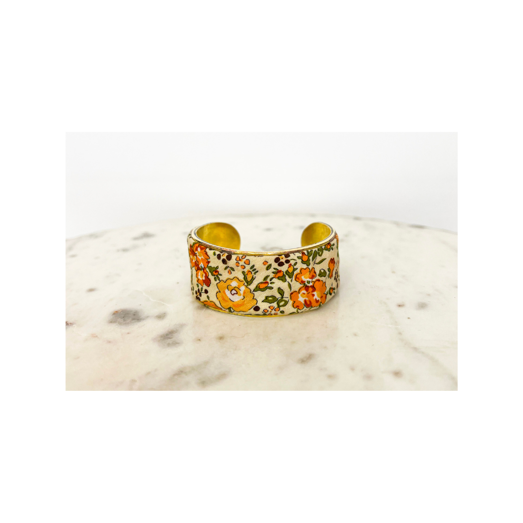 A gold floral cuff bracelet with a colorful design on a white background, displayed elegantly on a white surface.