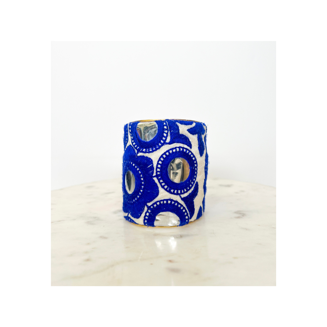 A wide band fabric bracelet, now featuring delicate blue circular patterns against a white background, lies gracefully on a light marble surface. This stylish piece captures the essence of a Spring Floral Cuff Bracelet with its charming design.