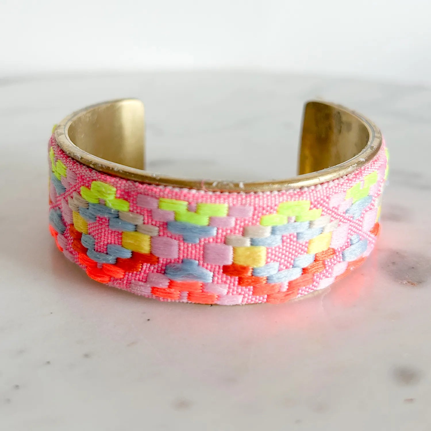 A 1-inch brass cuff bracelet from Redd Dott Jewelry with pink fabric embroidered in vibrant geometric shapes using neon pink, yellow, blue, and orange thread—an uplifting piece of embroidered jewelry and inspirational jewelry.