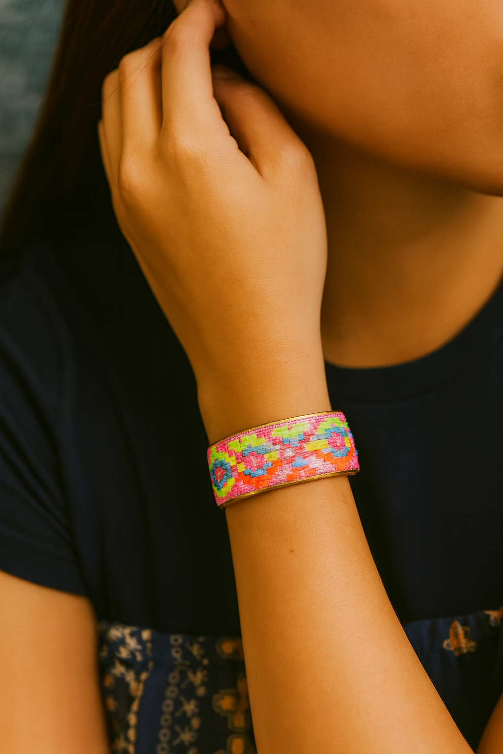 A person wearing the Abigail brass cuff bracelet along with beaded bracelets and gold rings, showing off the embroidered pink and neon geometric design in a playful, casual summer outfit—vivid and meaningful inspirational jewelry.