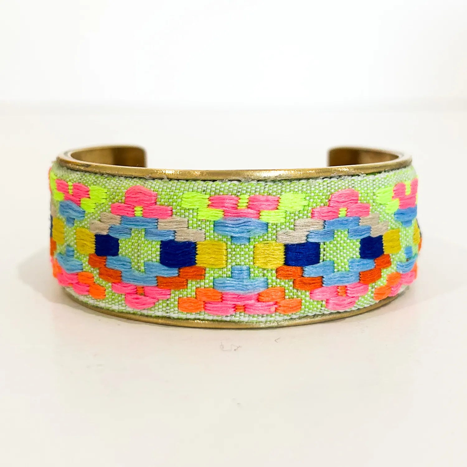 A 1-inch brass cuff bracelet from Redd Dott Jewelry featuring a woven lime green base with bright geometric patterns in neon pink, yellow, blue, and orange—an eye-catching geometric bracelet and piece of inspirational jewelry.