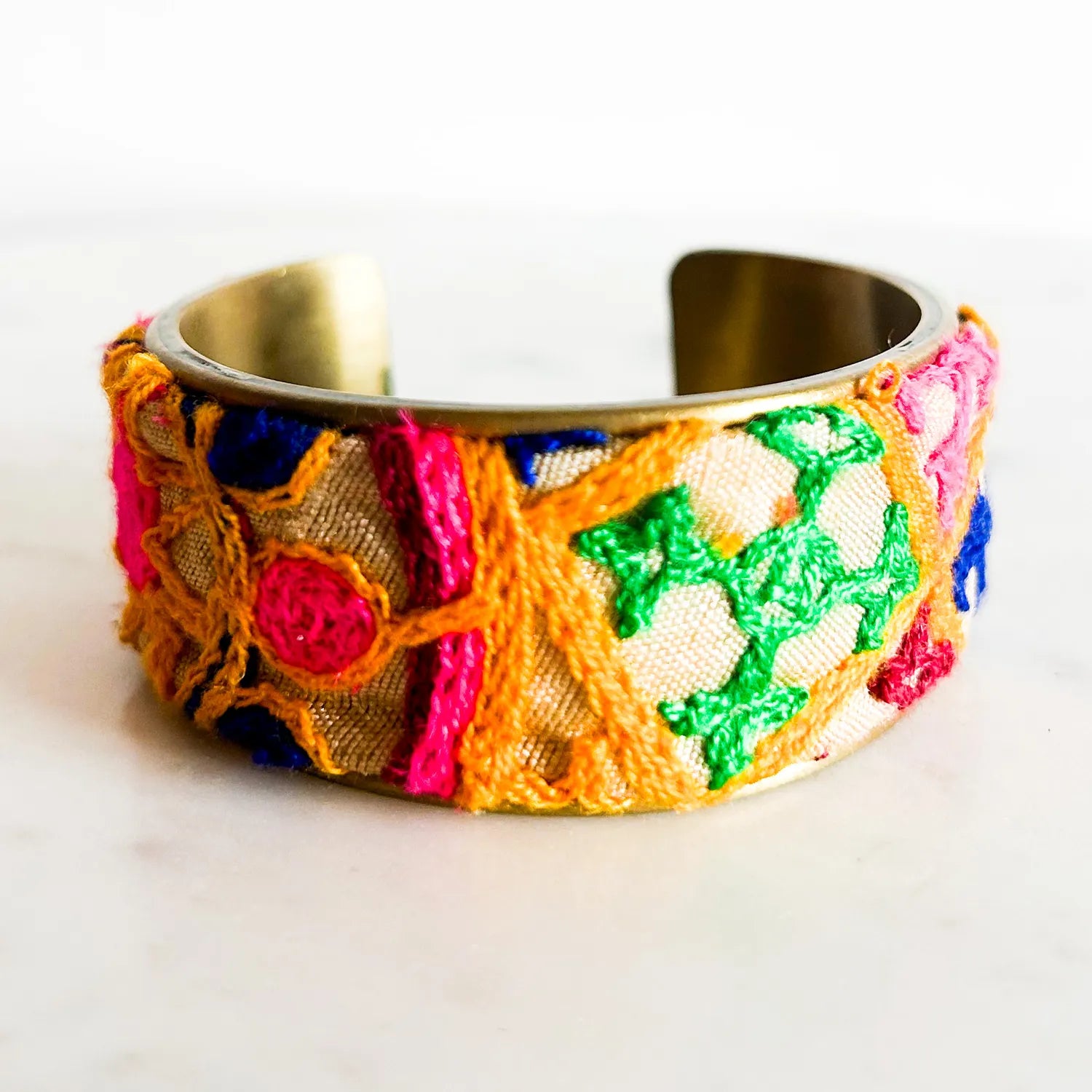 An open-back view of the Anika cuff showing its raw brass interior and linen exterior with multicolor medallion embroidery, highlighting both the 1-inch and 3-inch width options side by side on a white surface.