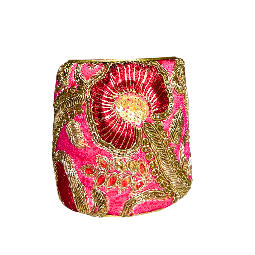 A handcrafted brass cuff bracelet by Redd Dott Jewelry featuring bold gold floral embroidery on vibrant hot pink fabric. A striking and elegant hot pink bracelet.