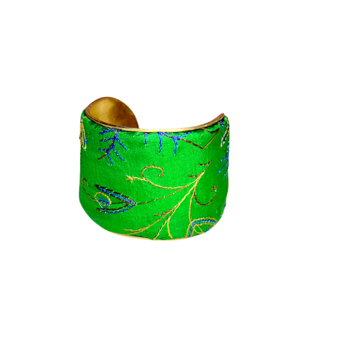 A handmade brass cuff bracelet from Redd Dott Jewelry, crafted and stamped in Shreveport, LA. Wrapped in green silk with gold and blue embroidered vines, this nature inspired jewelry piece features a botanical motif over a vintage brass base.