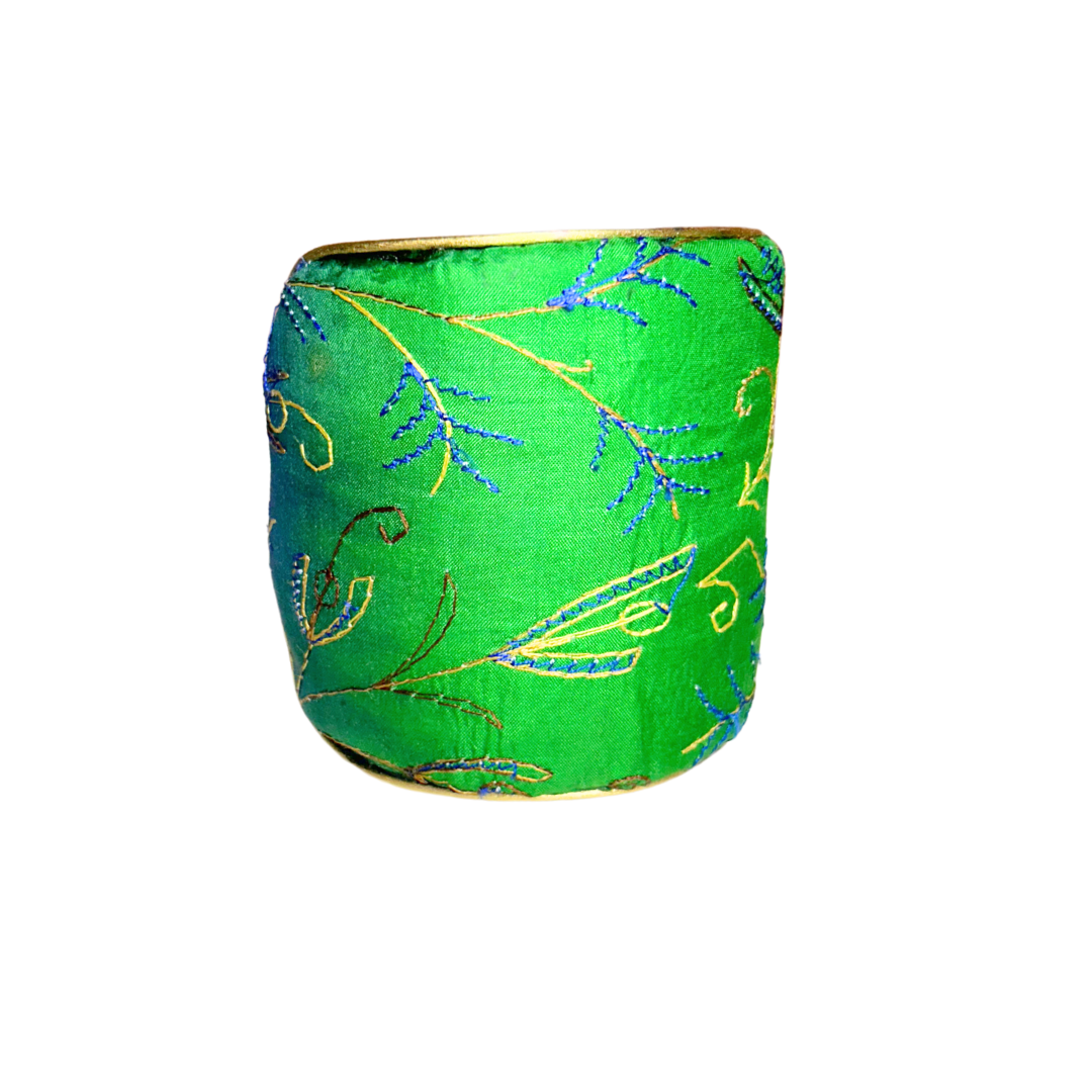 A handmade brass cuff bracelet from Redd Dott Jewelry, crafted and stamped in Shreveport, LA. Wrapped in green silk with gold and blue embroidered vines, this nature inspired jewelry piece features a botanical motif over a vintage brass base.