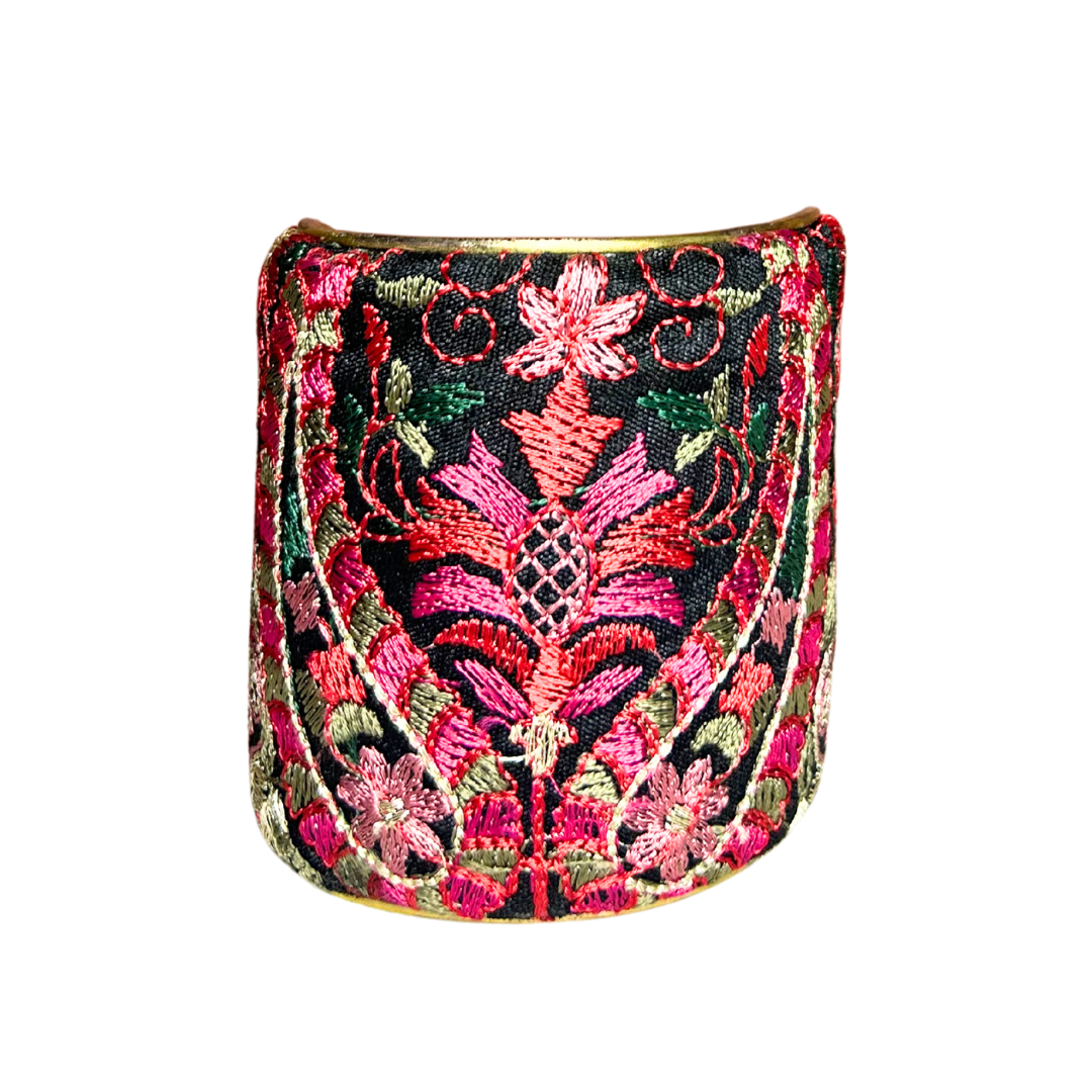 A handcrafted brass cuff bracelet by Redd Dott Jewelry featuring intricate hot pink and floral embroidery on a black background. A vibrant and ornate hot pink bracelet with elegant detailing.