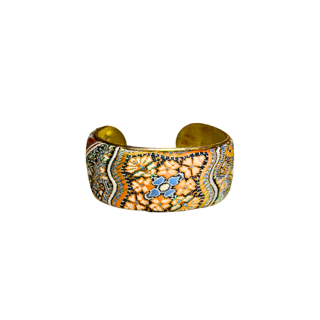 A handmade brass cuff bracelet from Redd Dott Jewelry, crafted and stamped in Shreveport, LA. Features an intricate mosaic-like fabric pattern in terracotta, blue, green, and cream over a vintage brass bracelet base.