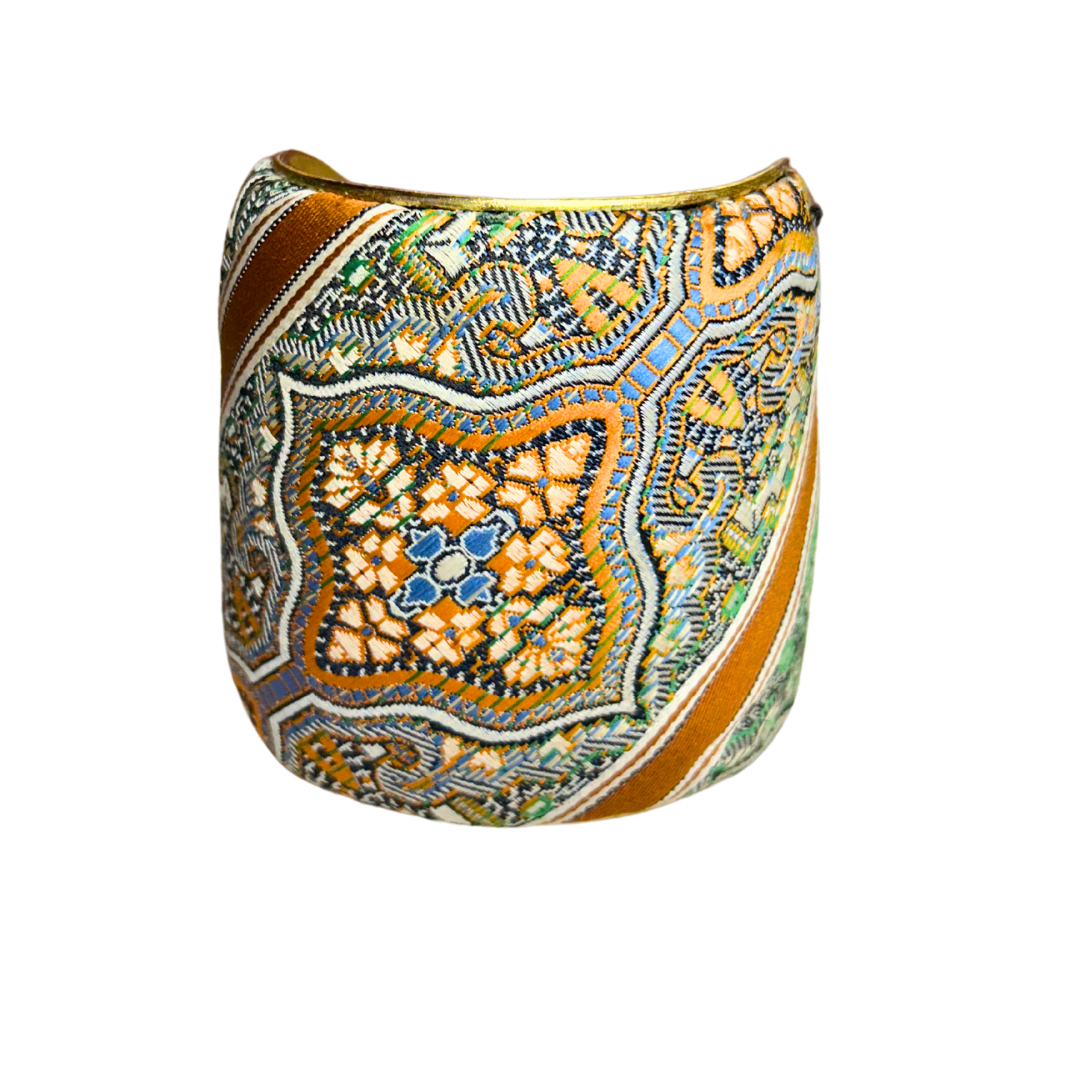 A handmade brass cuff bracelet from Redd Dott Jewelry, crafted and stamped in Shreveport, LA. Features an intricate mosaic-like fabric pattern in terracotta, blue, green, and cream over a vintage brass bracelet base.