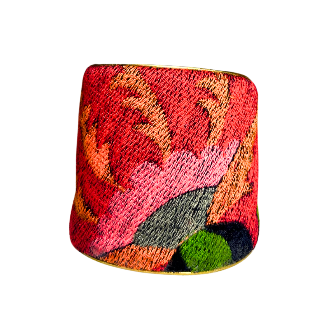 A handcrafted brass cuff bracelet by Redd Dott Jewelry with embroidered red, pink, and green floral motifs. A bold and vibrant piece of nature inspired jewelry.