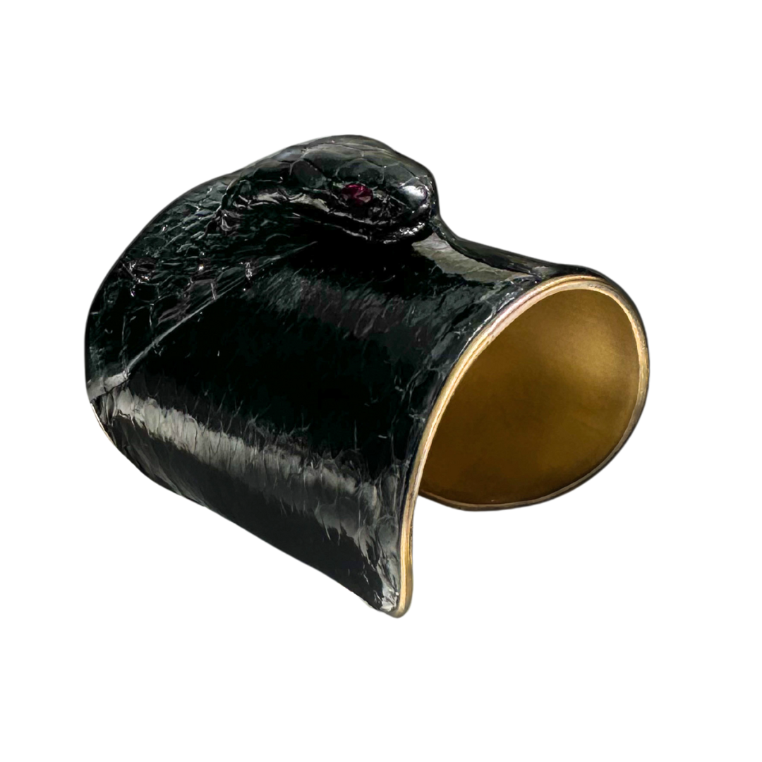Front view of cobra snake skin cuff bracelet with deep onyx scales and ruby eyes, polished brass interior, and high-gloss finish; one of a kind jewelry design.