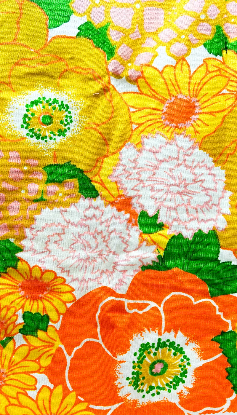 Close-up of Helen custom floral cuff bracelet fabric – oversized retro flowers in orange, yellow, white, and pink with green leaf accents on vintage textile used for brass cuffs.