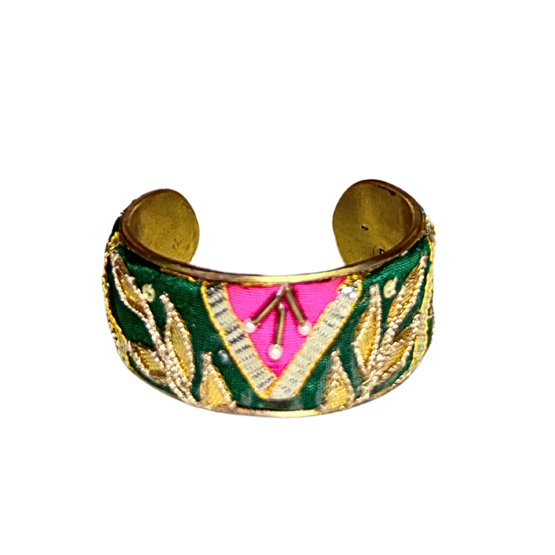 A handcrafted brass cuff bracelet by Redd Dott Jewelry with emerald green fabric and a vivid pink arrow design framed by metallic leaves. A bold, uplifting piece of inspirational jewelry.