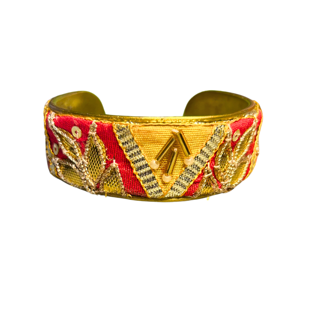 A handcrafted brass cuff bracelet by Redd Dott Jewelry featuring a bold orange base with metallic embroidery and directional arrow detailing. A vibrant piece of inspirational jewelry.