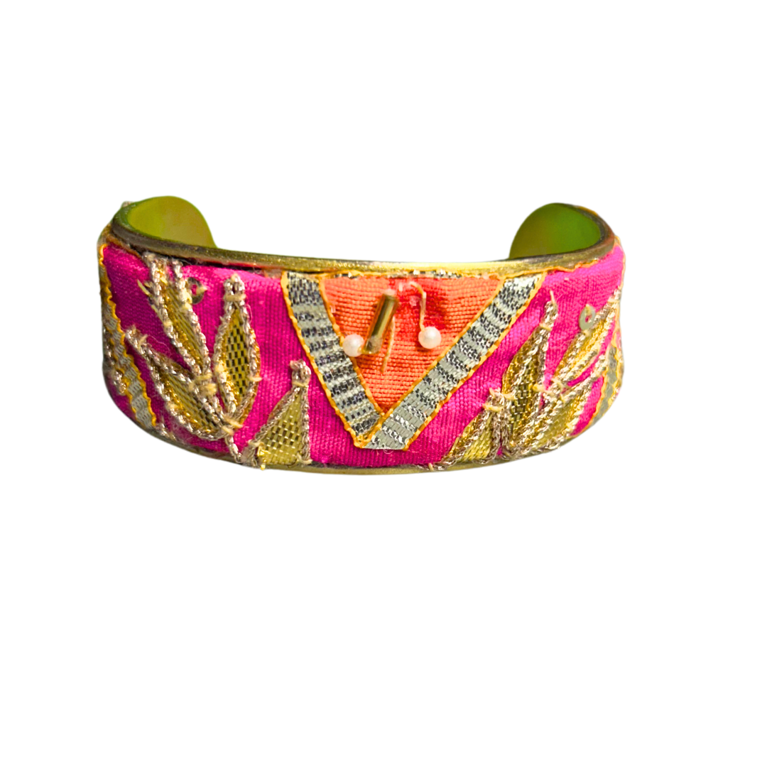 A handcrafted brass cuff bracelet by Redd Dott Jewelry with hot pink fabric, gold-threaded arrows, and sequin embellishments. A rich and symbolic piece of inspirational jewelry.