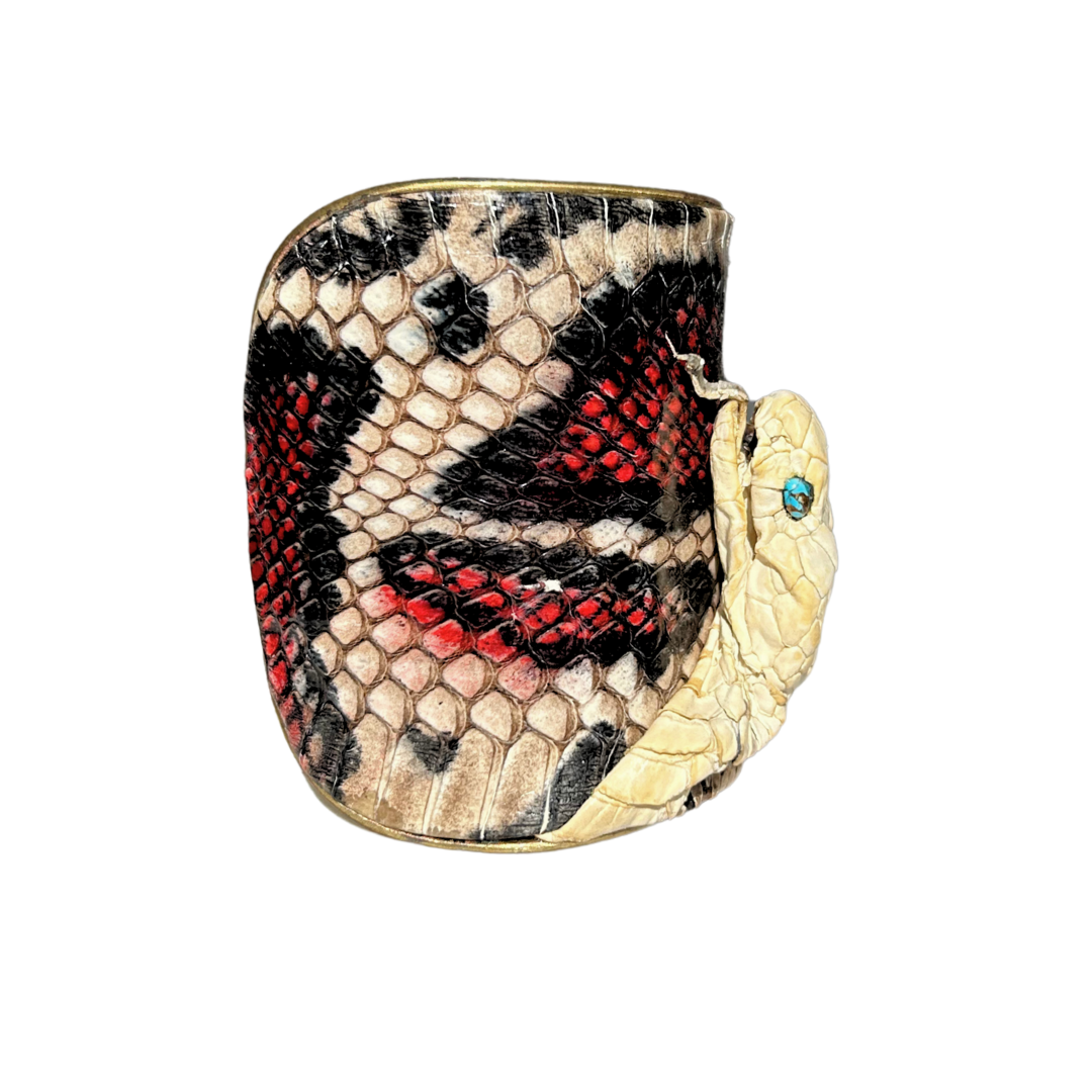 Left side view of A 3-Inch handcrafted nature inspired jewelry cuff bracelet by Redd Dott Jewelry featuring real king cobra skin in black, ivory, and red, with a cobra head detailed with genuine turquoise eyes. Fierce, sculptural, and richly textured.